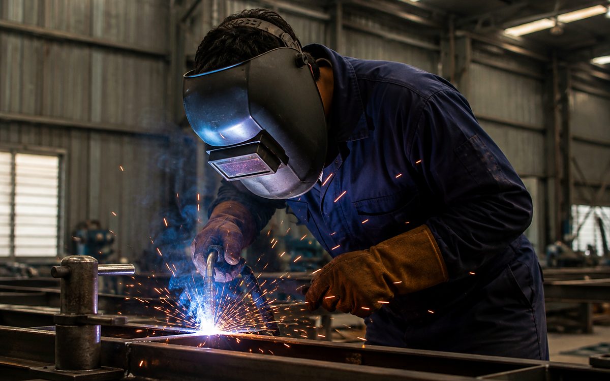 A welder in a protective helmet working on a steel section, sparks flying from the joint
