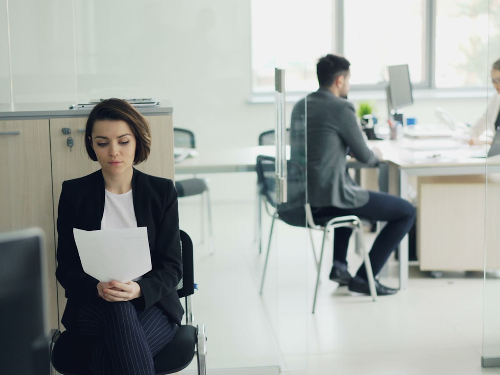 A woman holding papers in an open plan office, colleagues working behind her
